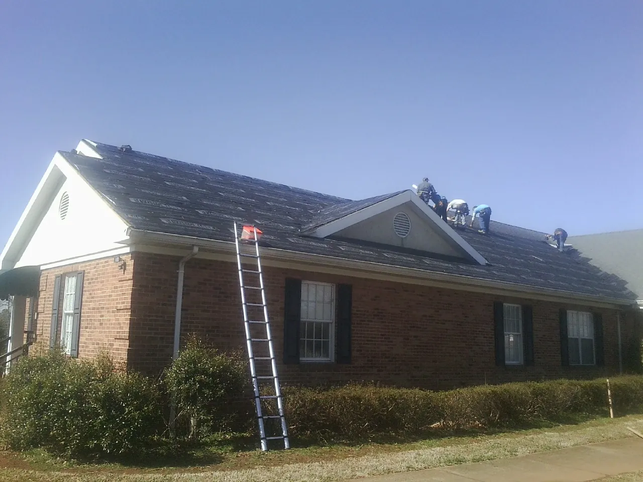 Crew tearing shingles off a brick ranch roof with a ladder set — Metal Roof Repair work by our crew in Tyngsboro