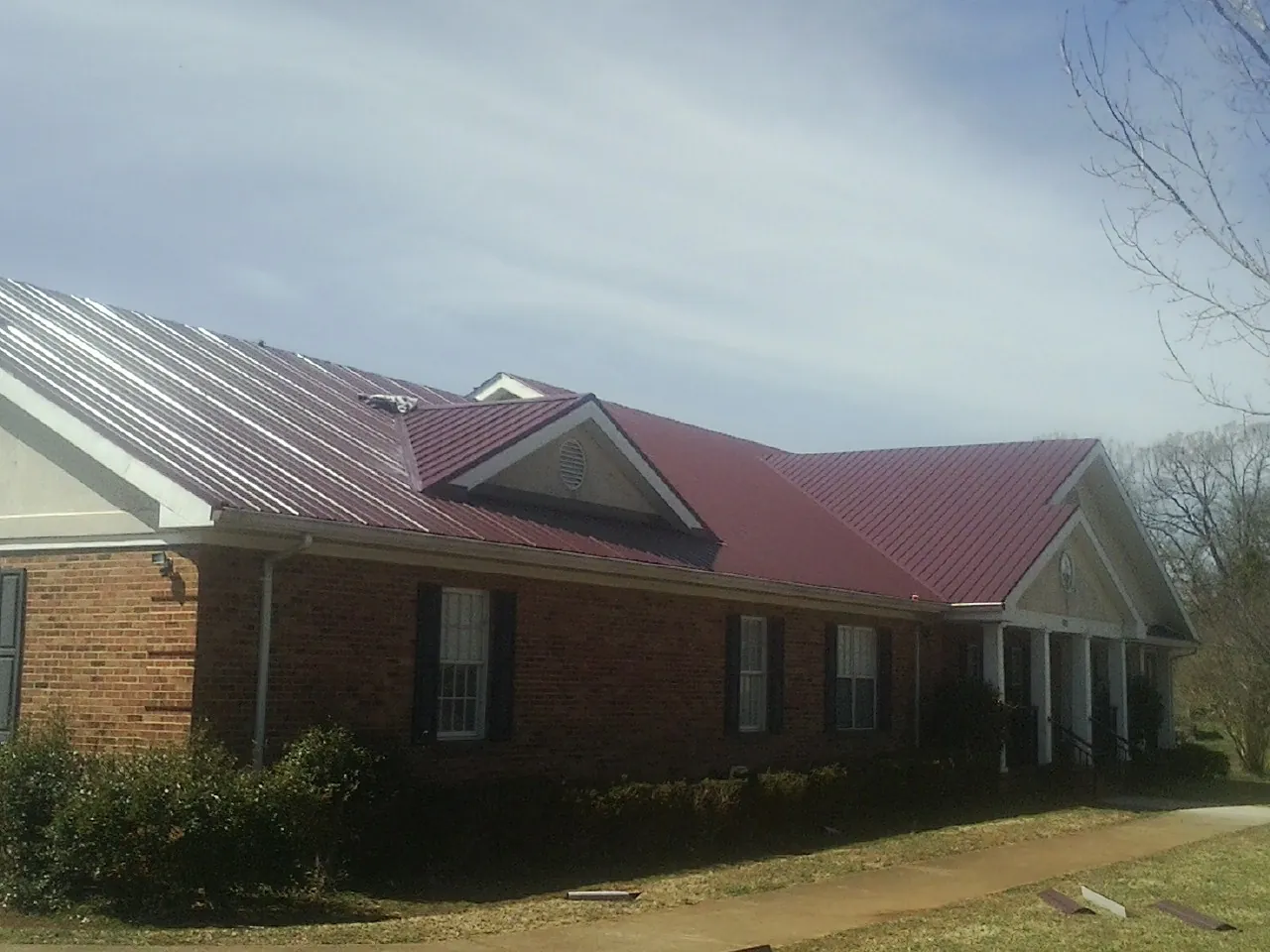 Red metal roof with gabled entries on a long brick building, from a Hail Damage Roof Repair job in Tyngsboro