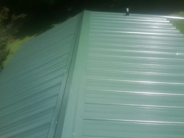 New green metal panels meeting at the ridge of a roof — Flat Roof Repair work by our crew in Tyngsboro