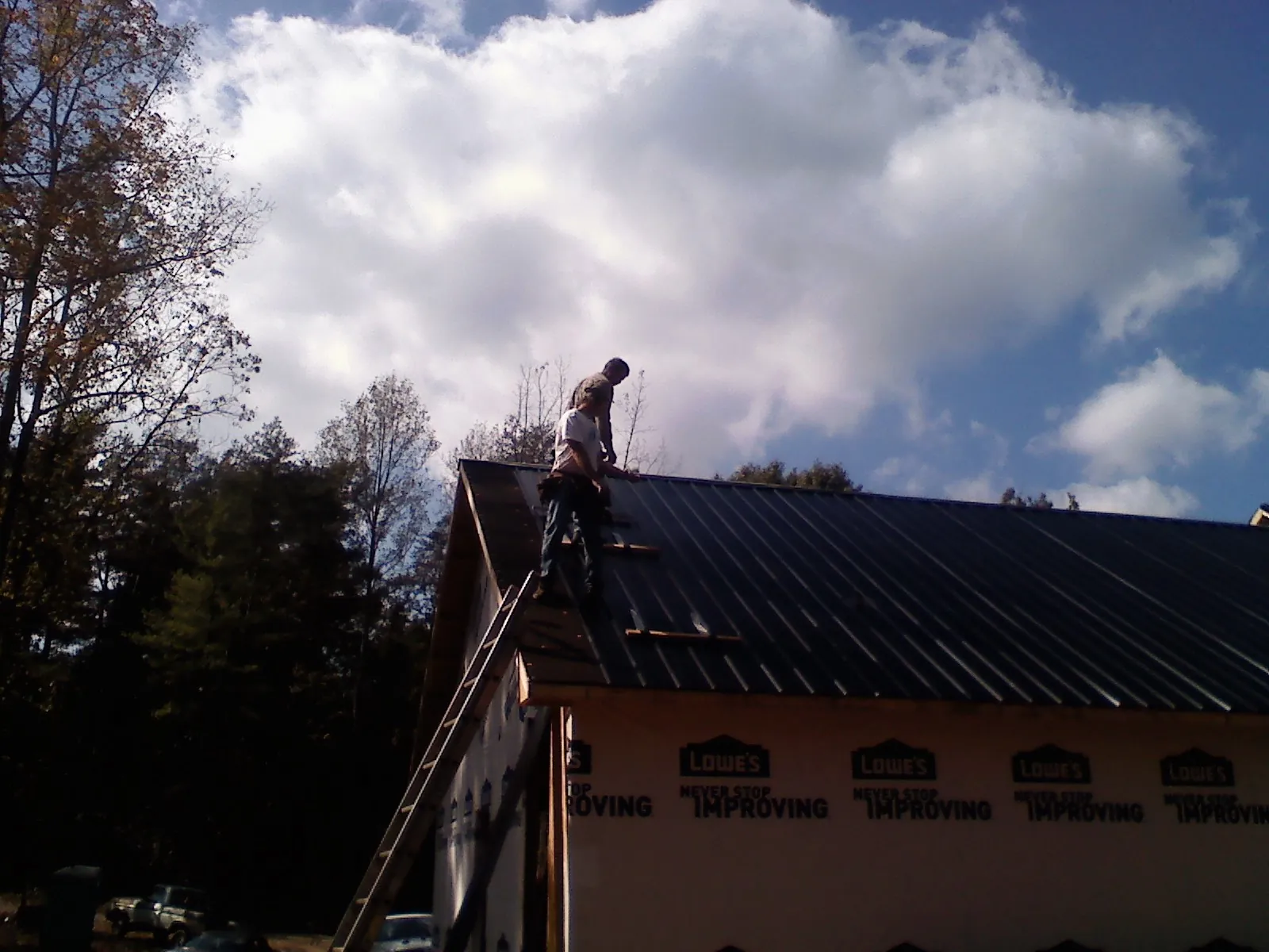Roofer fastening dark metal panels high against a cloudy sky, from a Roof Inspection job in Tyngsboro