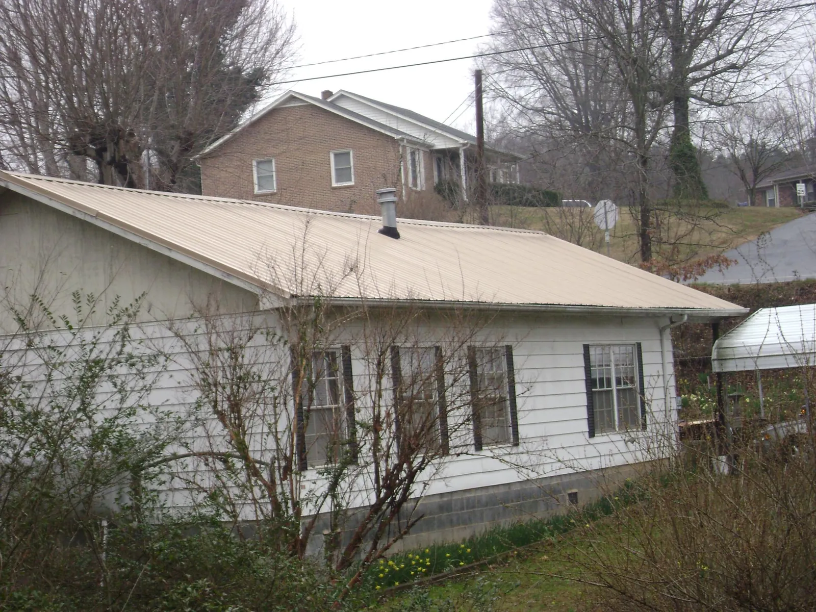 Tan metal roof on a white sided house set into a hillside — Commercial Roofing by Roofing Brothers in Tyngsboro