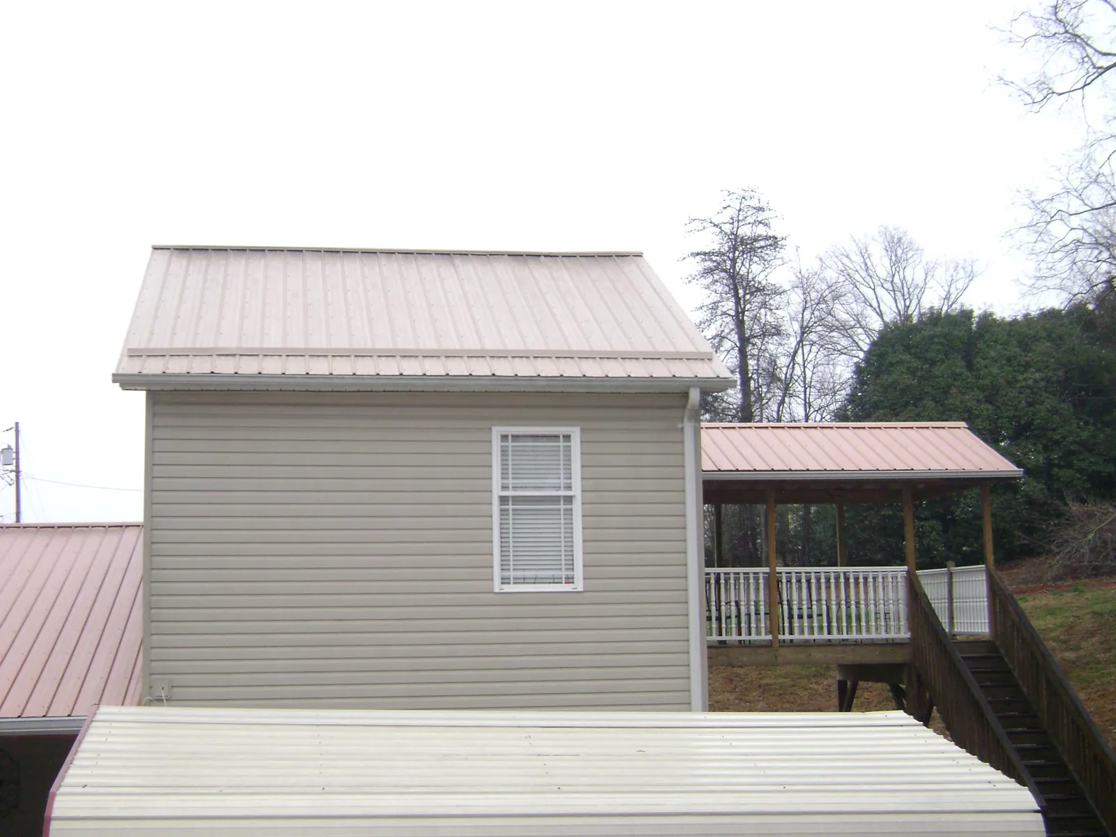Tan metal roofs on a two story addition and attached porch, from a Roof Replacement job in Tyngsboro